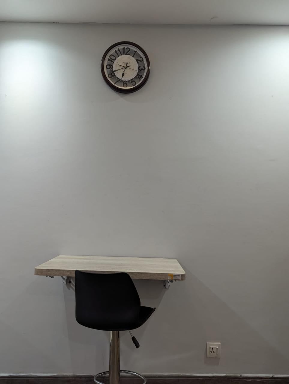 Compact work desk with a black chair and wall clock