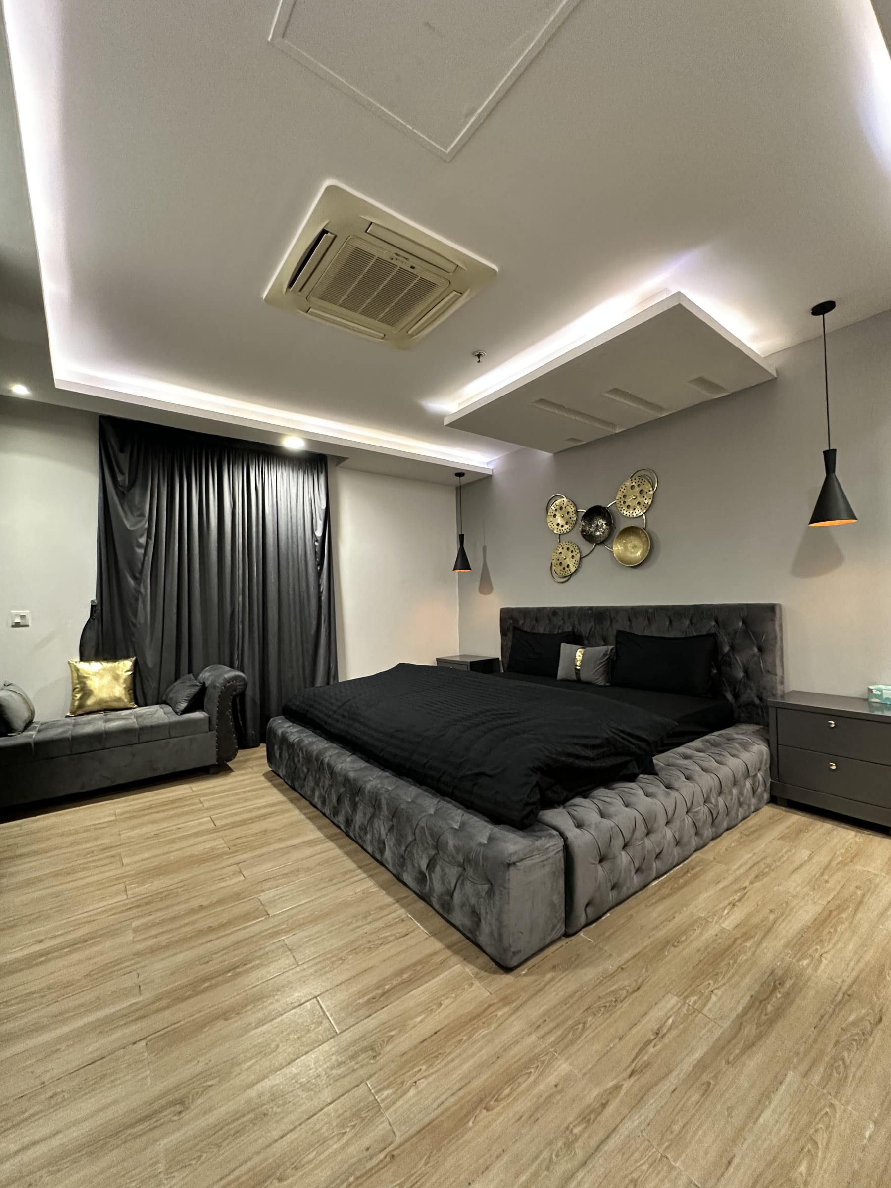 Bedroom with a grey upholstered bed, dark bedding and pendant lights