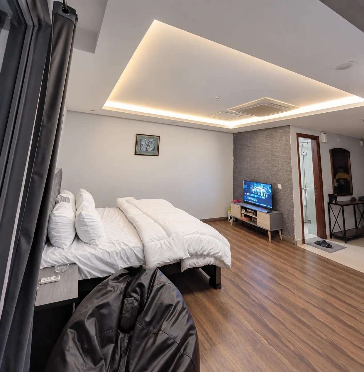 Studio sleeping and sitting space with white bedding, a television and grey curtains