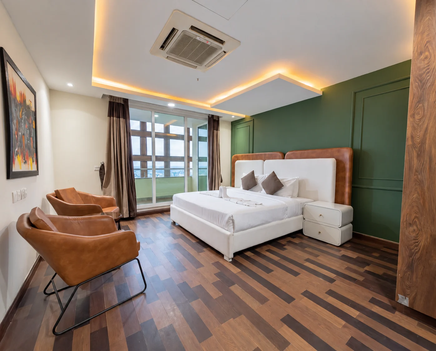 Bedroom with green panelling, a white bed and caramel-toned chairs beside the balcony