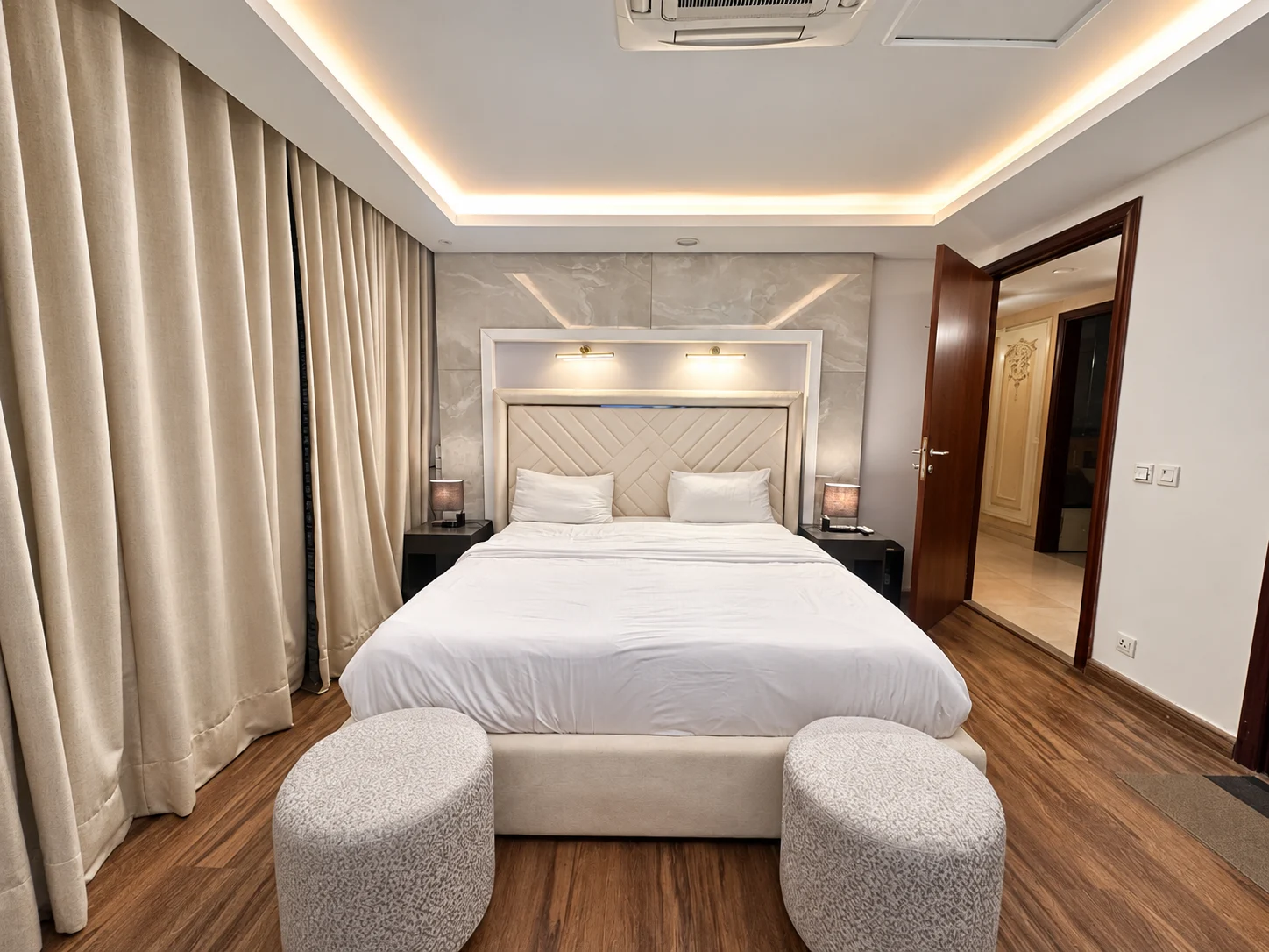 Bedroom with a white upholstered bed, twin ottomans and full-length curtains