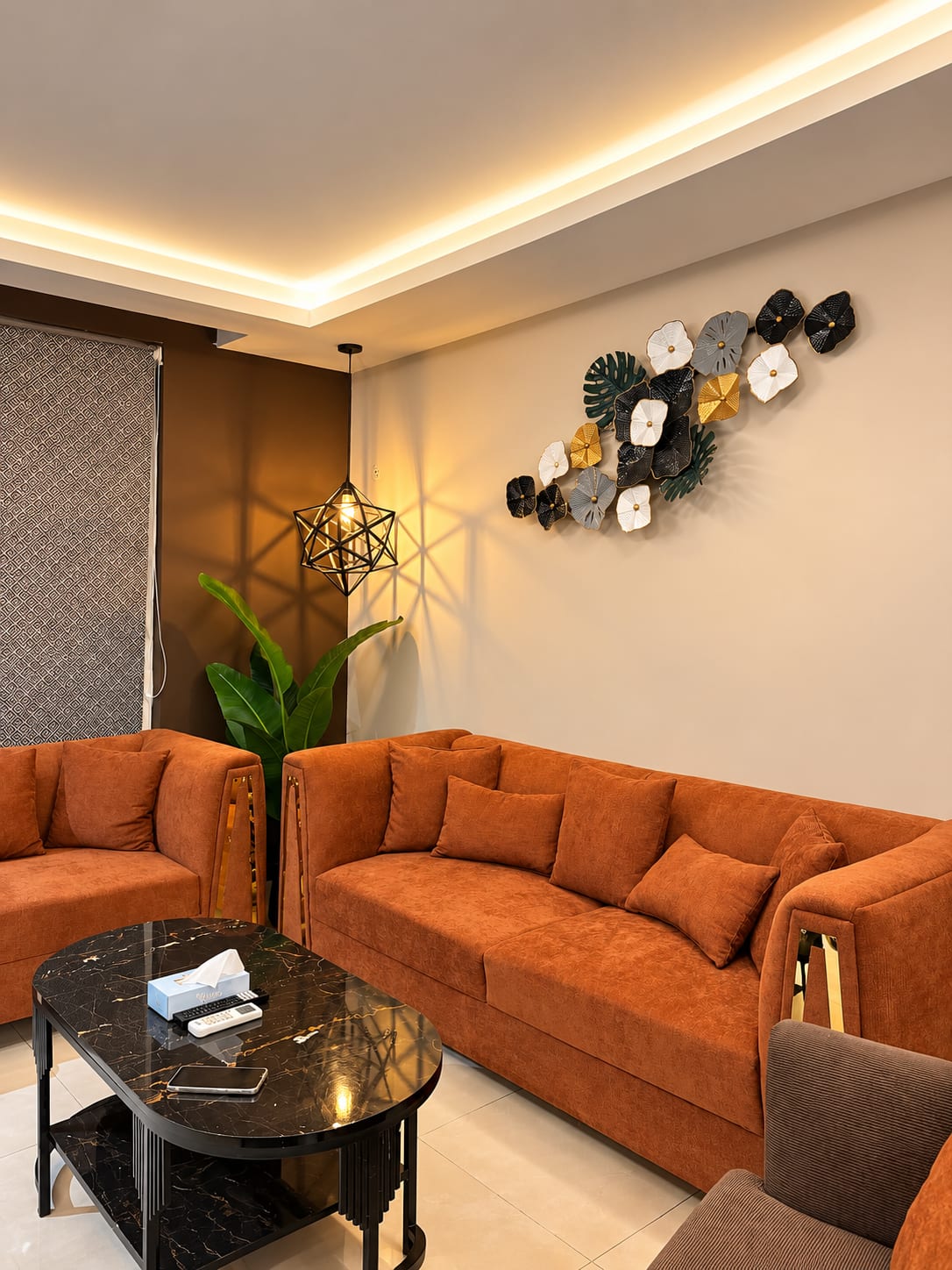 Rust-orange lounge sofas around a dark oval coffee table, with a plant beside the window
