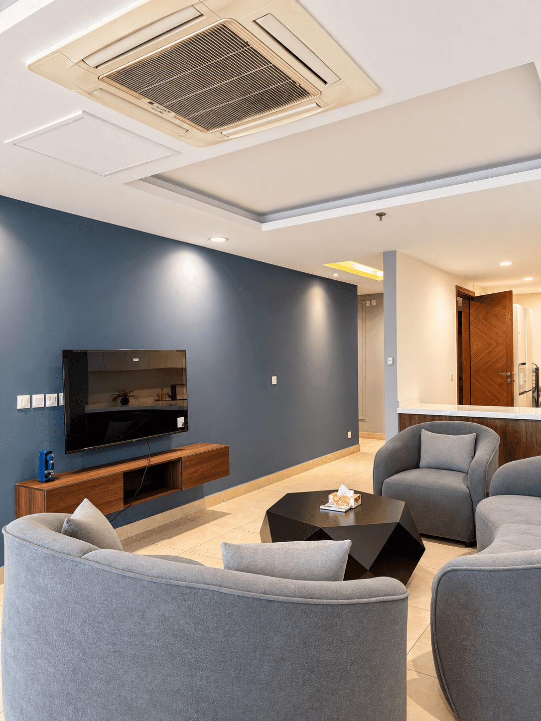Television and wooden console against the blue living-room wall, facing grey sofas and an armchair