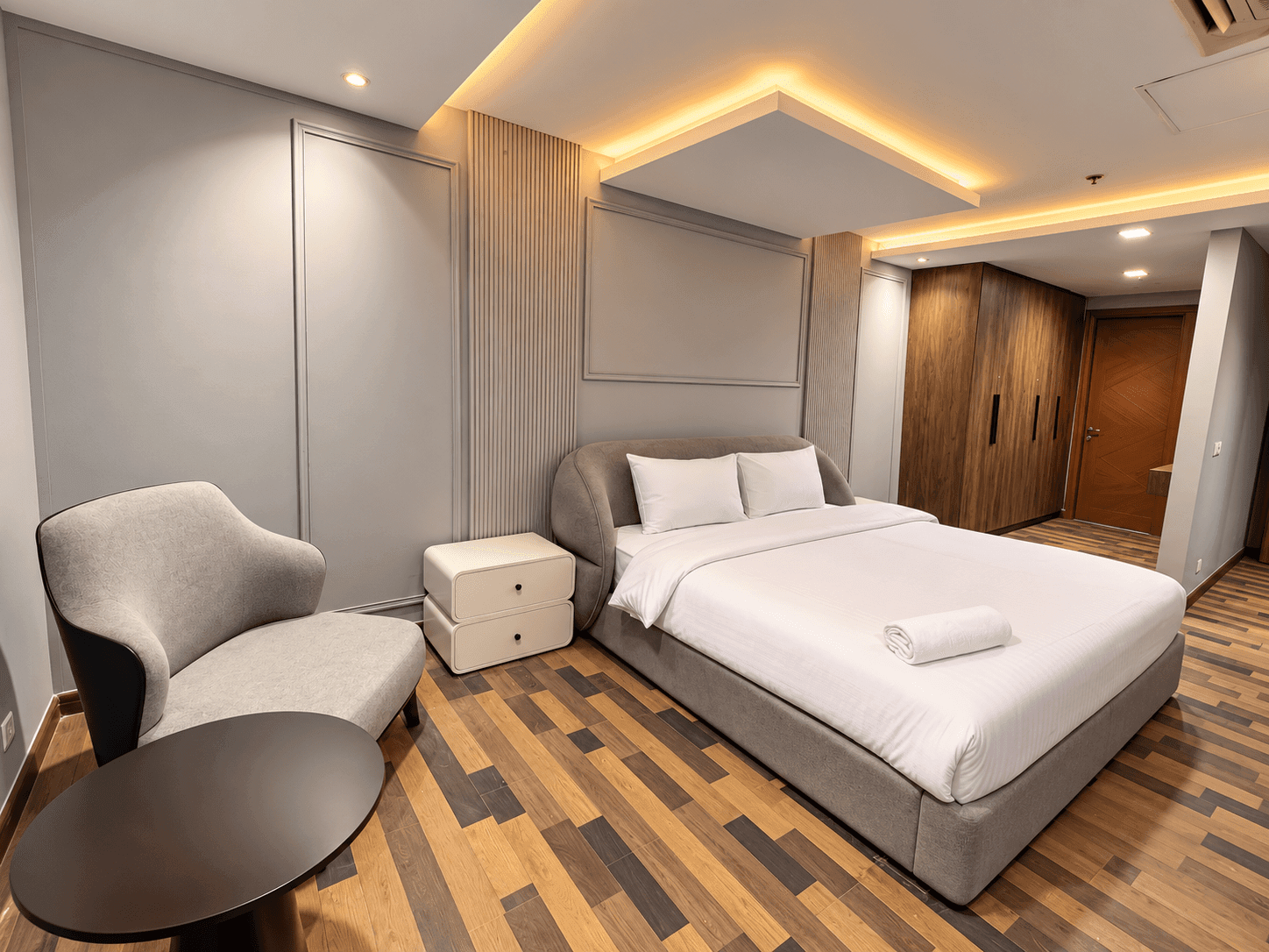 Bedroom with a grey upholstered bed, armchair, round side table and wooden wardrobe