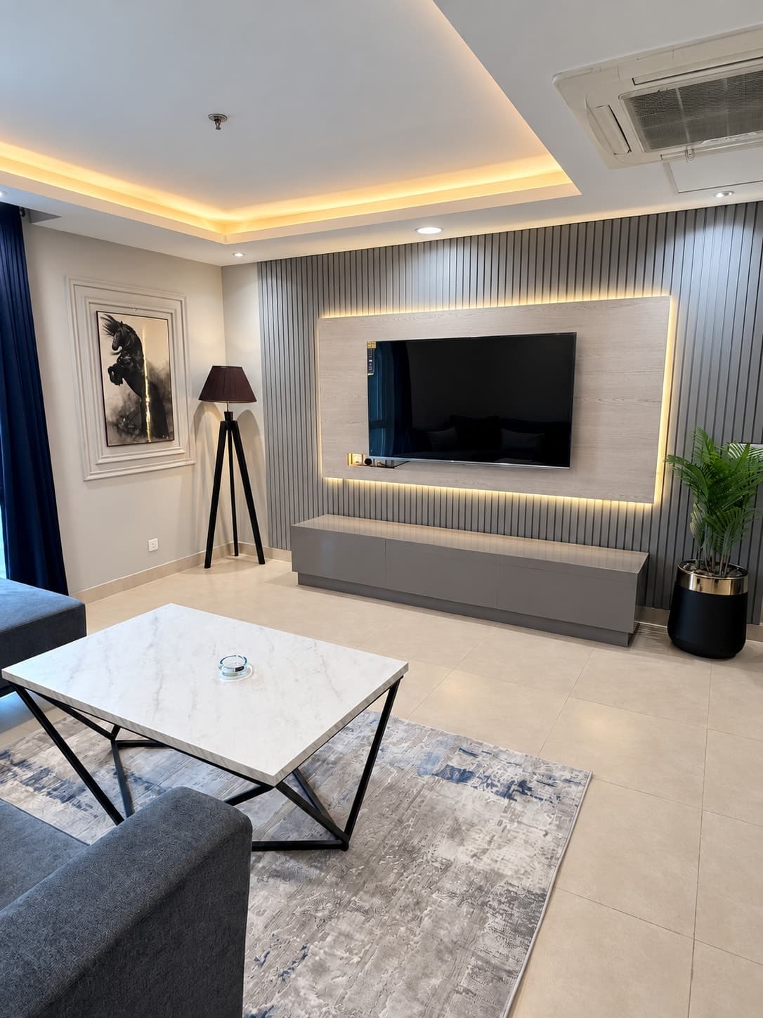 Backlit television wall and grey console facing the lounge coffee table, beside a tripod floor lamp and plant