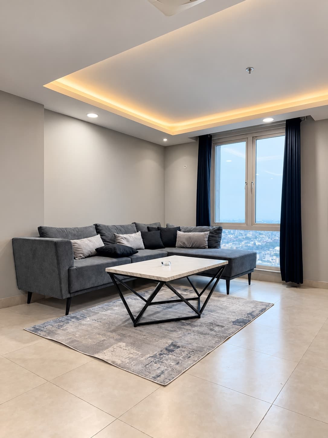 Charcoal sectional sofa and pale coffee table beside tall windows and dark curtains