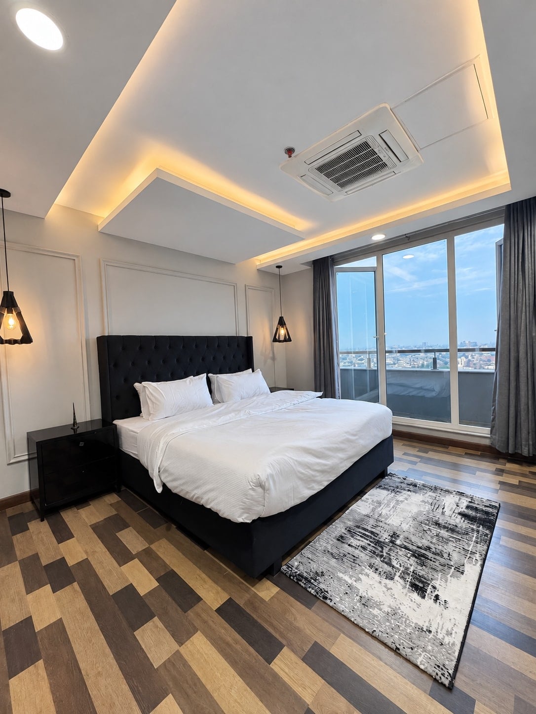 Bedroom with a dark upholstered bed, white linen and glass doors overlooking the balcony