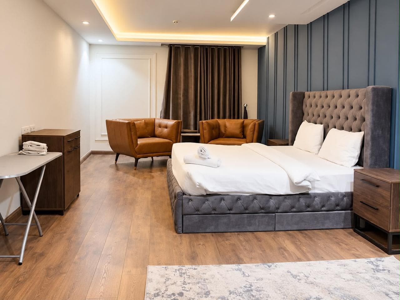 Bedroom with a grey tufted bed, blue wall panelling and two caramel-coloured armchairs