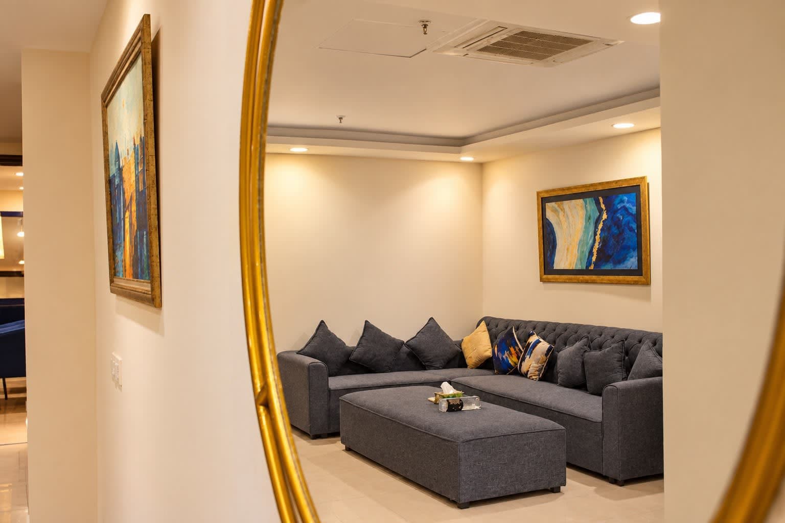 Gold-framed mirror reflecting the lounge seating, patterned cushions and blue abstract artwork