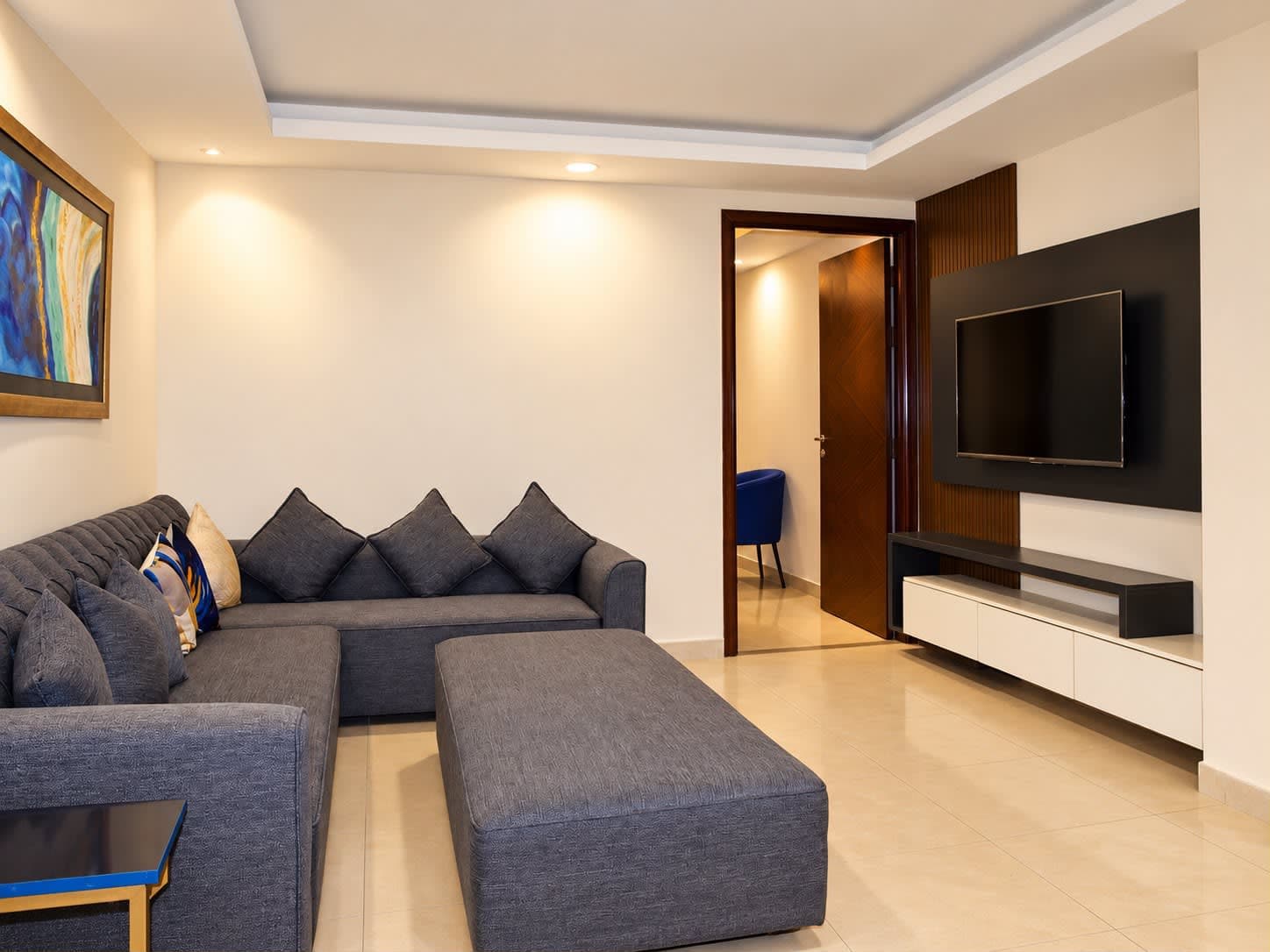 Separate lounge with a sectional sofa facing the television and a low white media cabinet