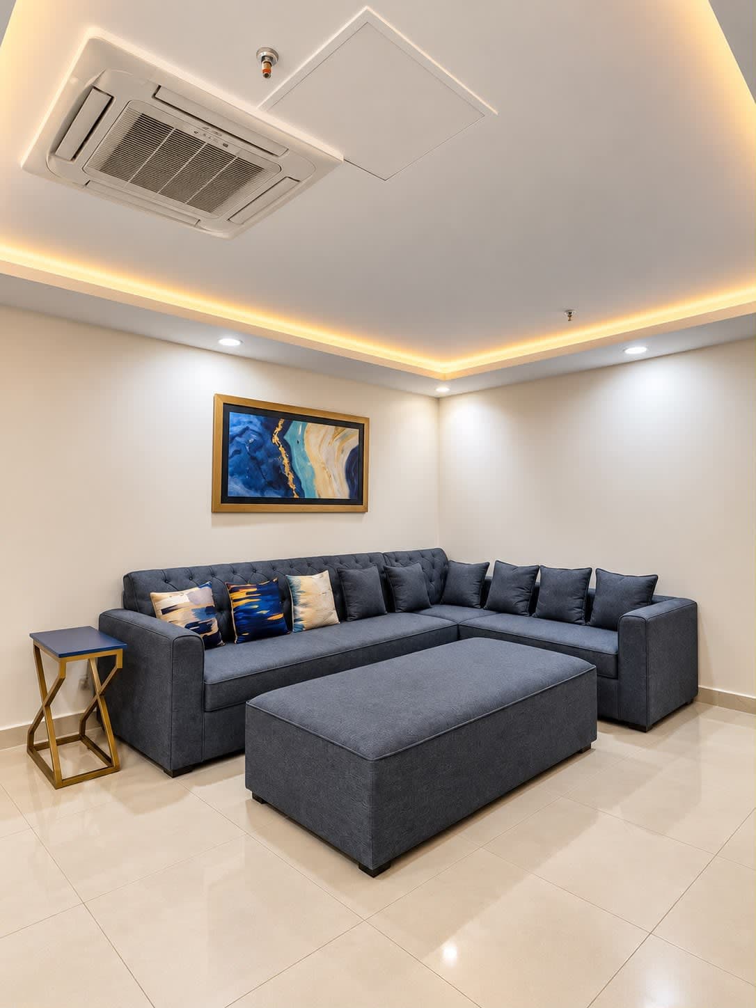 Blue-grey corner sofa and matching ottoman beneath blue abstract artwork and warm ceiling lighting