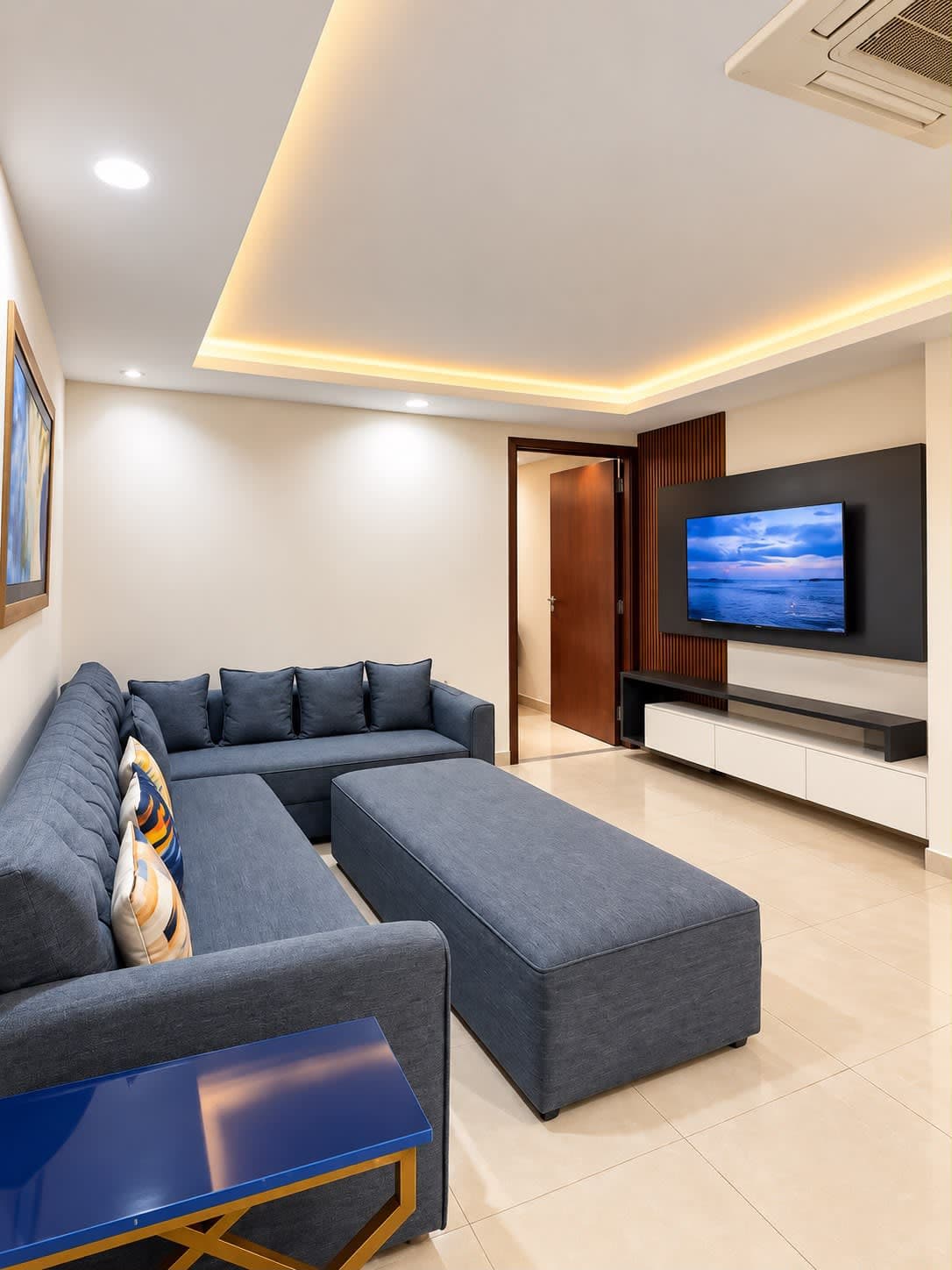 The Sapphire Suite lounge with blue-grey sectional seating, an upholstered ottoman and a wall-mounted television